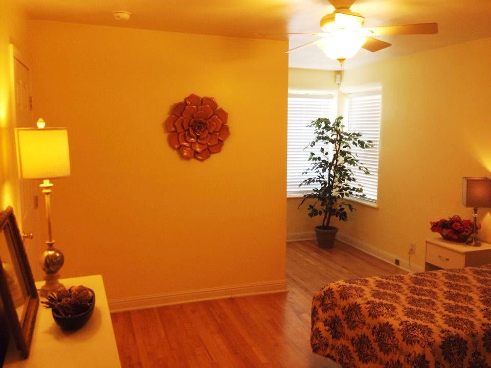 A cozy bedroom with warm lighting, featuring a ceiling fan and a potted plant by the window.