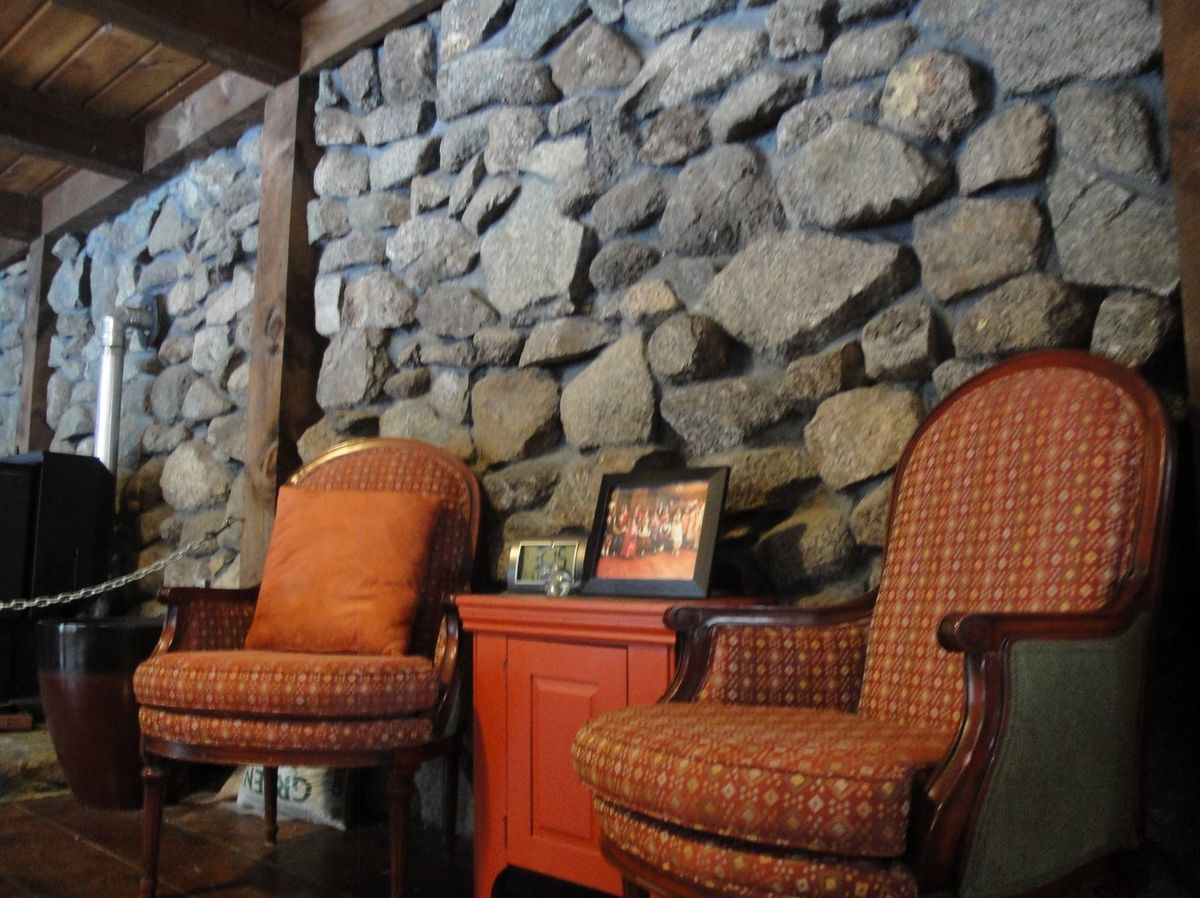 A cozy interior featuring a rustic stone wall, two comfortable chairs, and a side table.