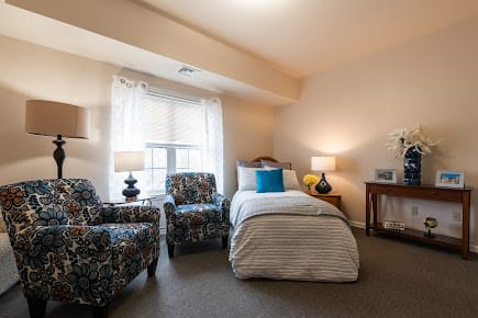 A cozy bedroom with a single bed, two patterned chairs, and soft lighting from table lamps.