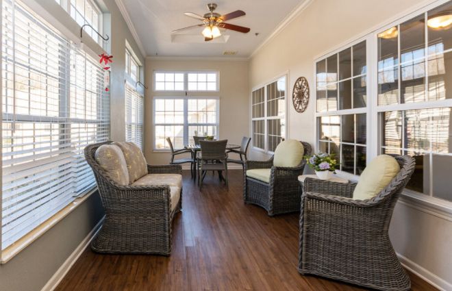 A cozy sunroom featuring wicker furniture, large windows, and a ceiling fan.