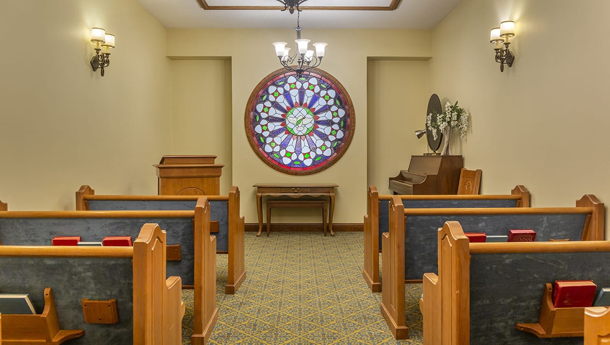 A small chapel with wooden pews and a decorative stained glass window.
