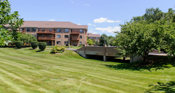A scenic view of an apartment complex with a well-maintained lawn and surrounding trees under a clear blue sky.