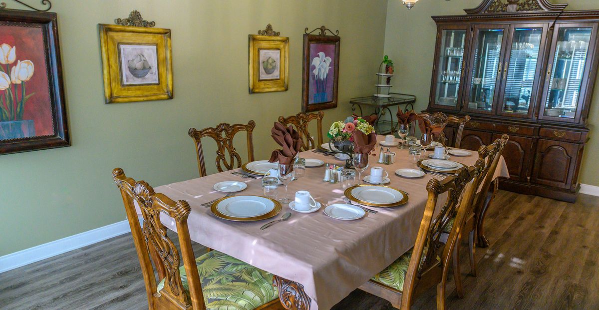 An elegantly set dining table with fine china, surrounded by ornate chairs and decorated with flowers and framed art.