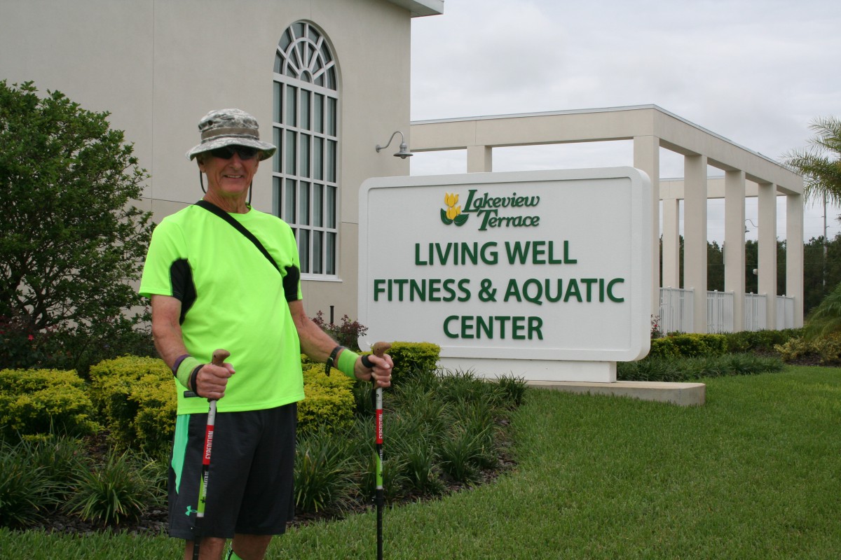 A person standing outside the Living Well Fitness & Aquatic Center holding walking poles.