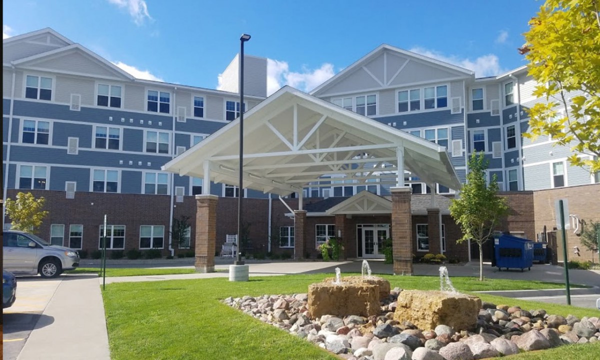 A large residential building with a covered entrance and landscaped front yard on a sunny day.