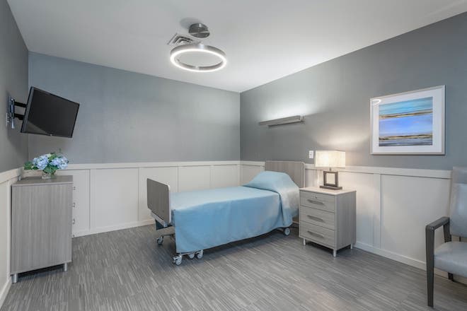 A clean and minimalist hospital room with a single bed and a nightstand.