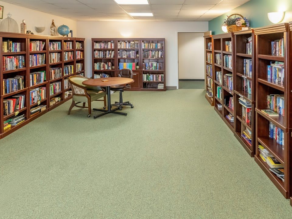 A quiet library room with shelves full of books and a table with chairs in the center.