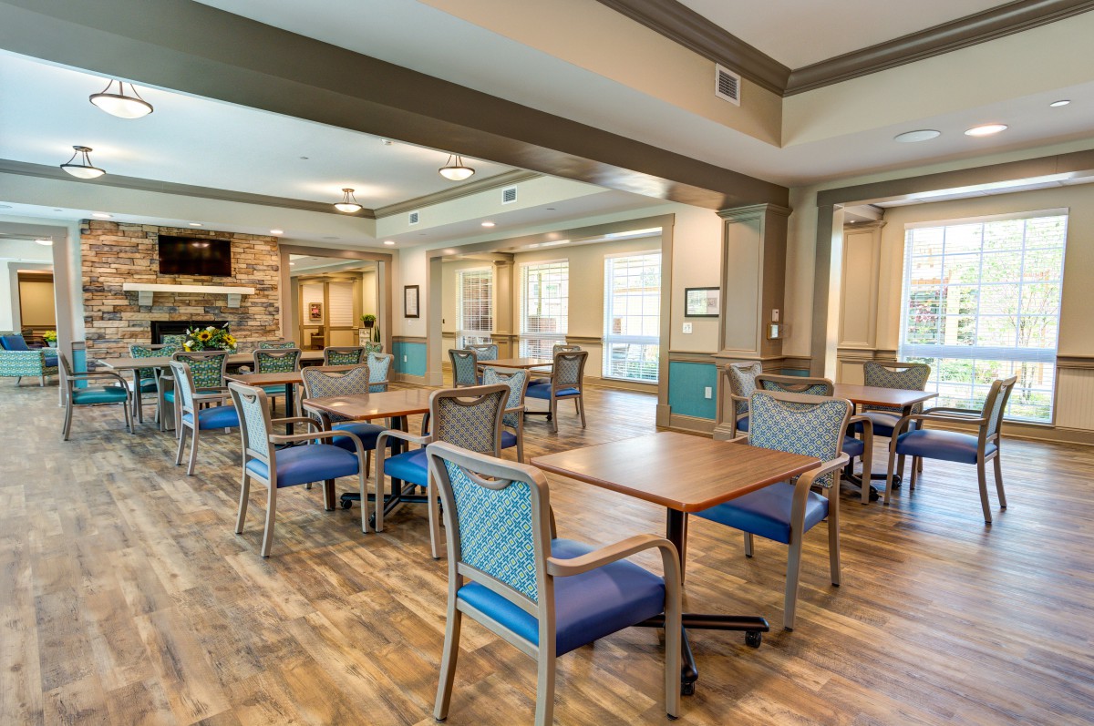 A spacious dining area with wooden floors, tables and chairs, well-lit by large windows.