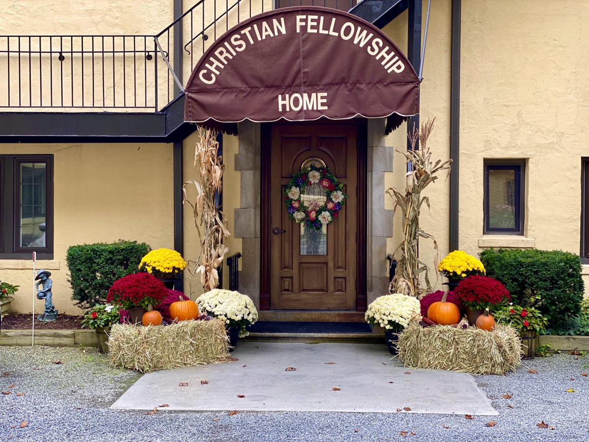 The entrance of a Christian fellowship home, adorned with autumn decorations including flowers, pumpkins, and hay bales.