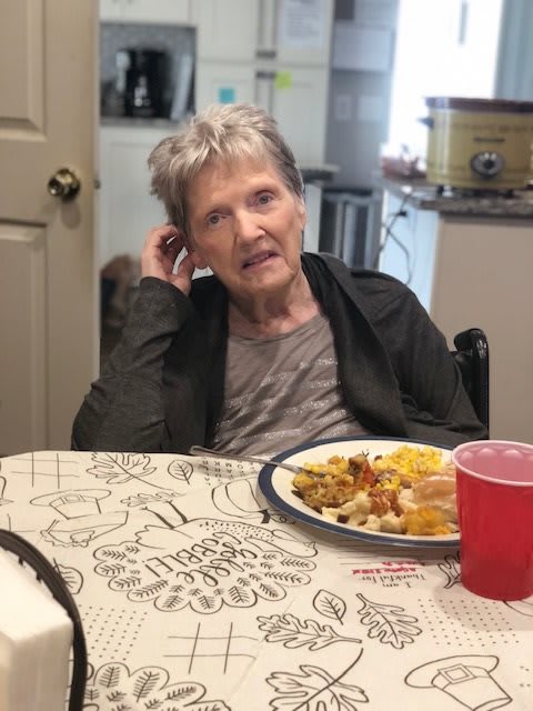 An elderly woman sitting at a table with a plate of food.