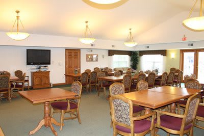 A spacious dining area with multiple tables and chairs, featuring a television and soft lighting.