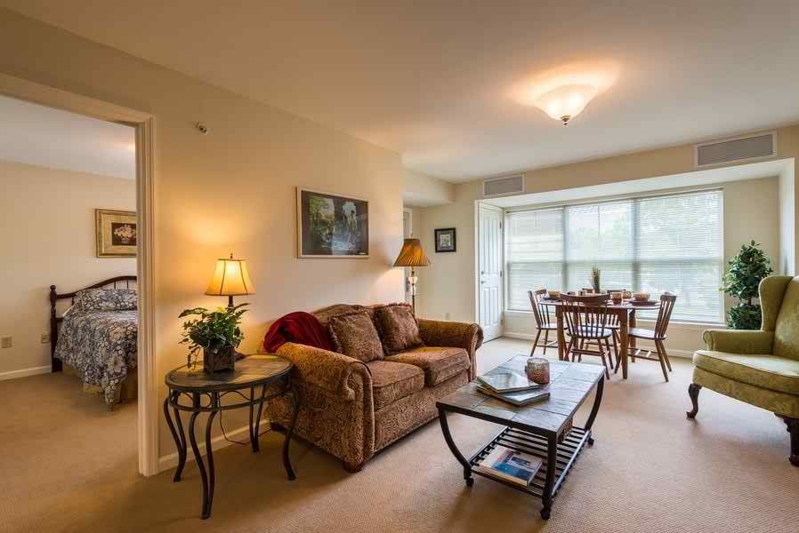 A cozy living room with a sofa and coffee table, leading to a dining area filled with natural light from large windows.
