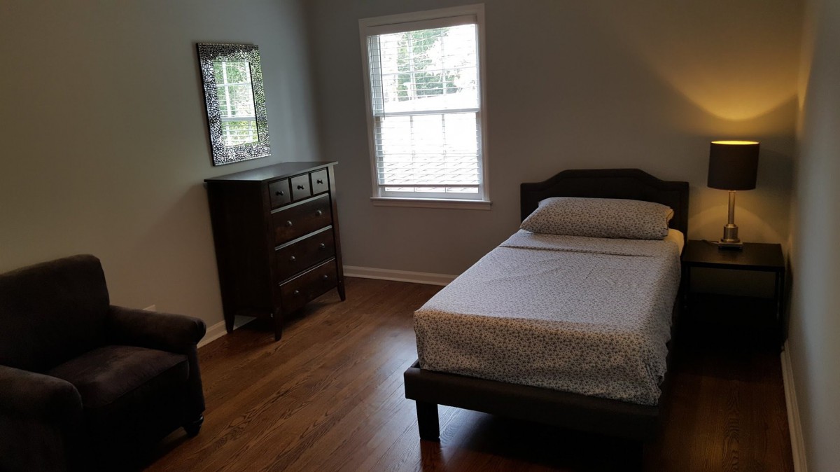 A simple bedroom with a single bed, dresser, and window lighting.