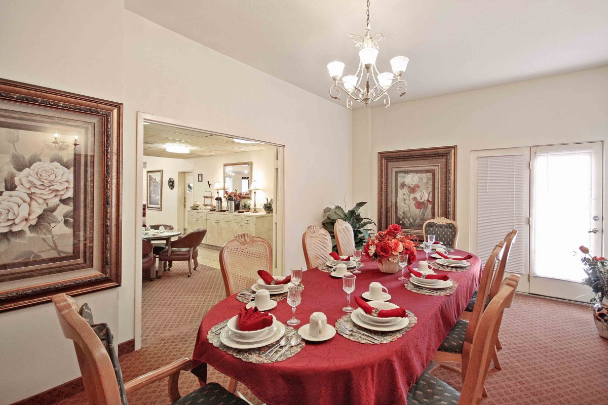 An elegant dining room with a table set for a meal, featuring a red tablecloth and adorned with decorative items.