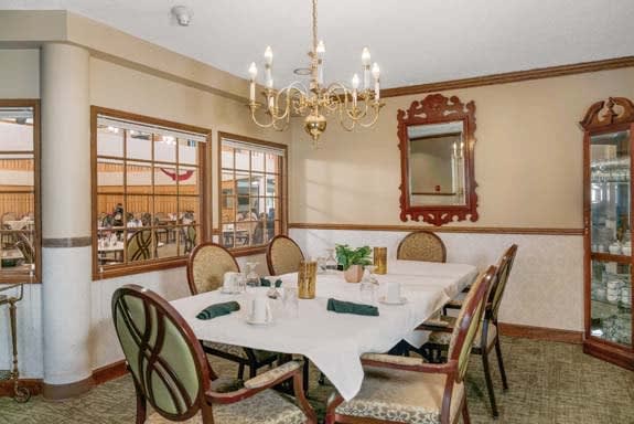 An elegant dining room with a set table, chandelier, and ornate mirror on the wall.