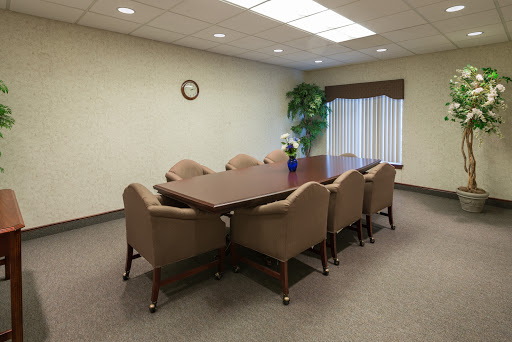 A spacious conference room featuring a large meeting table surrounded by comfortable brown chairs, complemented by a decorative plant and a wall clock.