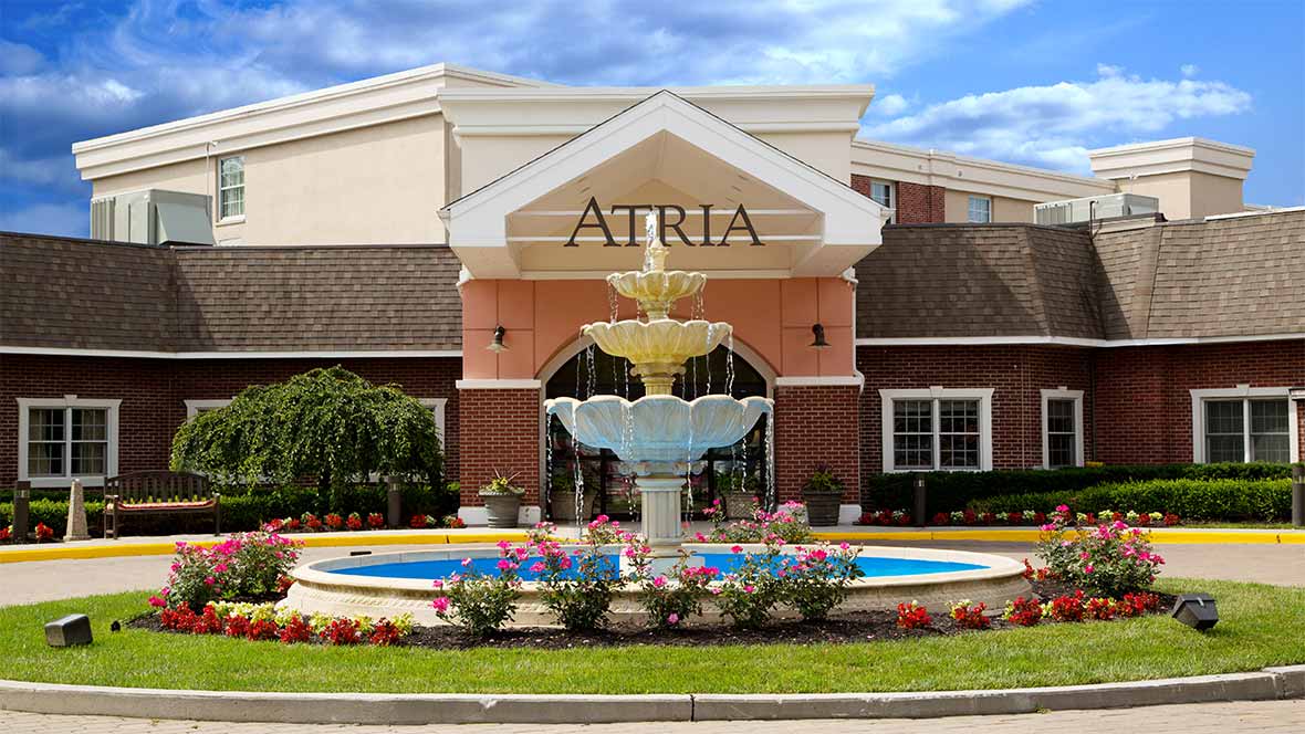 Atria retirement home entrance with a decorative fountain and landscaped flowers.