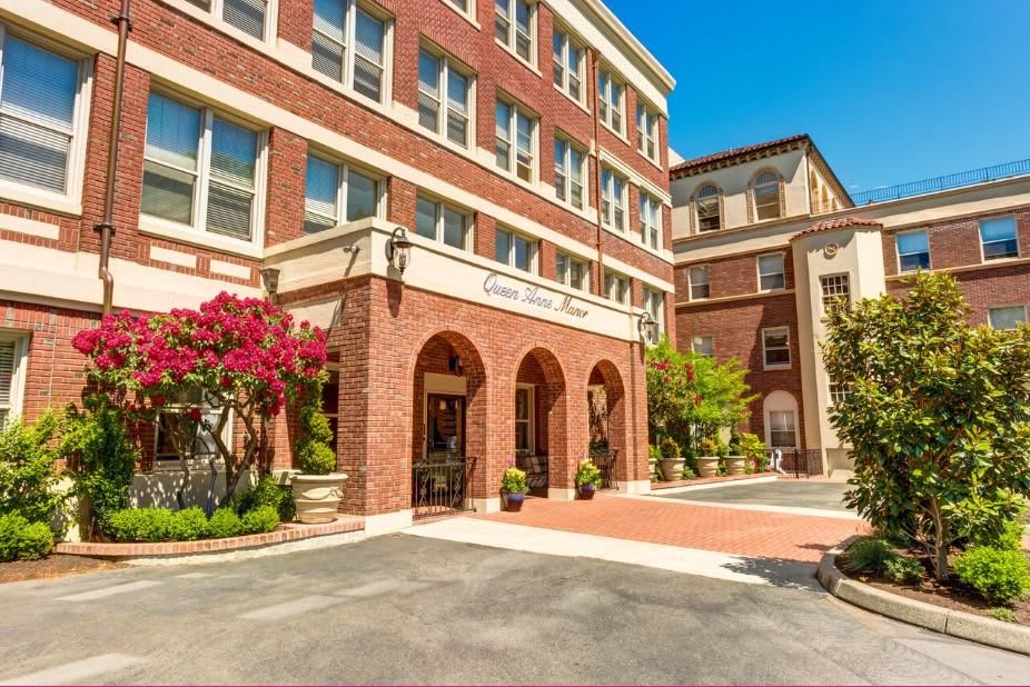A brick building with an arched entrance, surrounded by trees and landscaping on a sunny day.