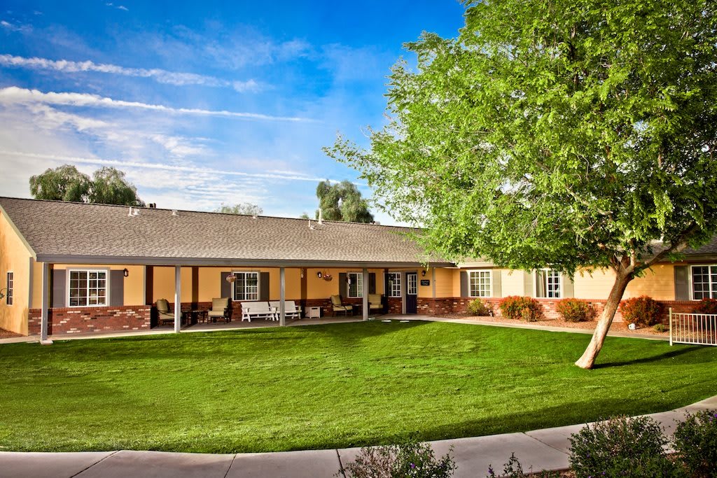 A single-story house with a well-maintained yard and lush green grass under a clear blue sky.