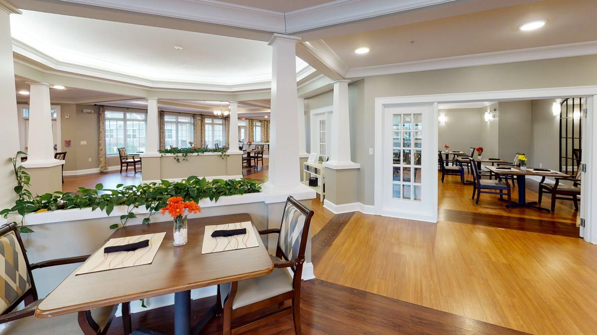 A spacious and elegantly designed dining area with wooden floors, tables, and chairs, complemented by decorative plants.