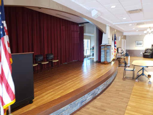 A view of a stage in an auditorium, featuring red curtains and a polished wooden floor.