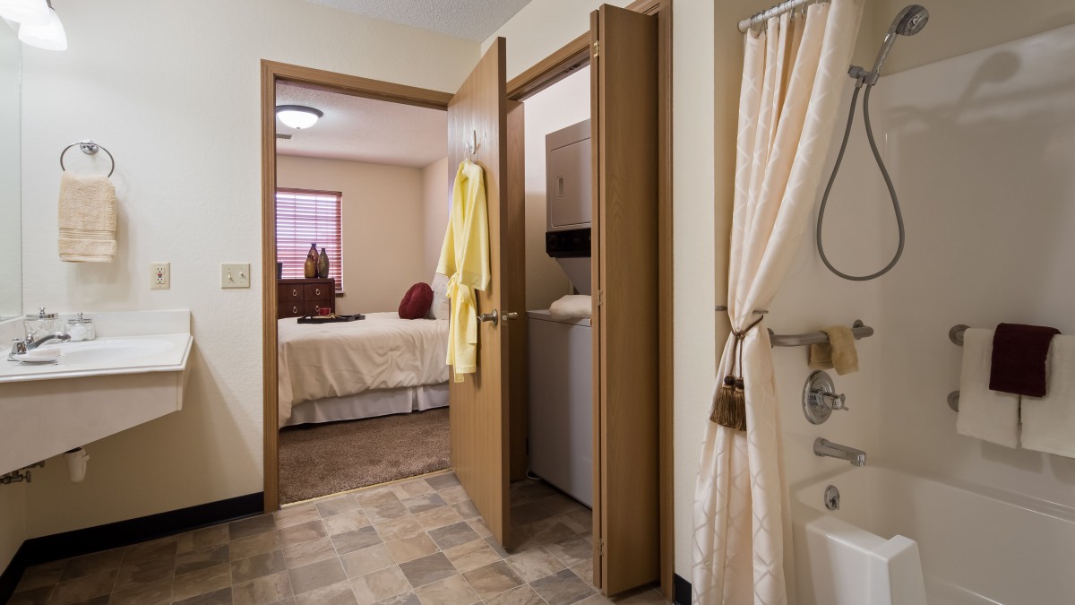 A cozy view of a modern bathroom leading into a bedroom, featuring a hanging robe and shower curtain.