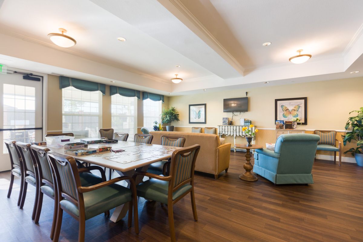 A spacious living room with a table and chairs, sofas, large windows, and a television.