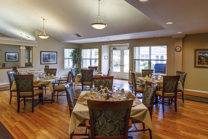 A well-lit dining area with neatly arranged tables and chairs, featuring elegant decor and hardwood flooring.