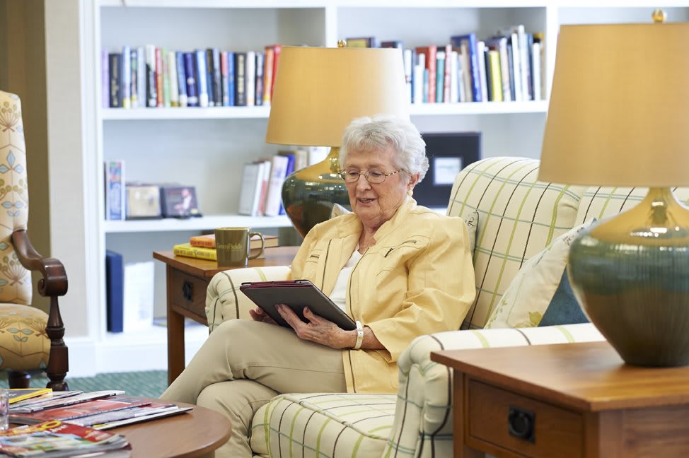 An elderly woman reading on a tablet in a cozy living room.