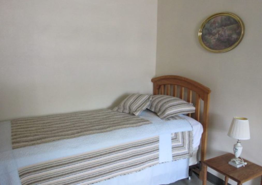 A simple bedroom setup with a single bed featuring striped bedding, a wooden headboard, and wall decor.