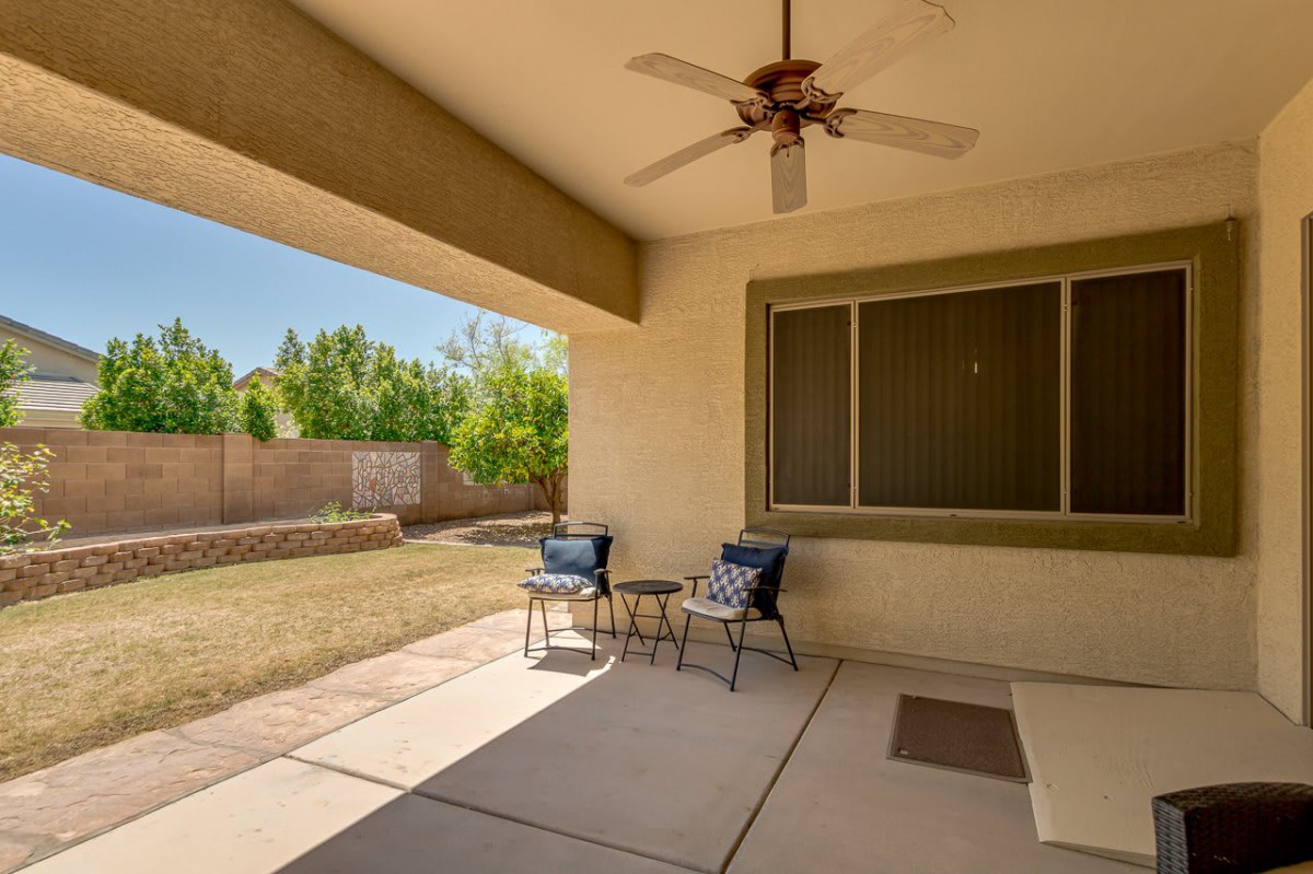A covered patio with seating and a ceiling fan overlooks a backyard.