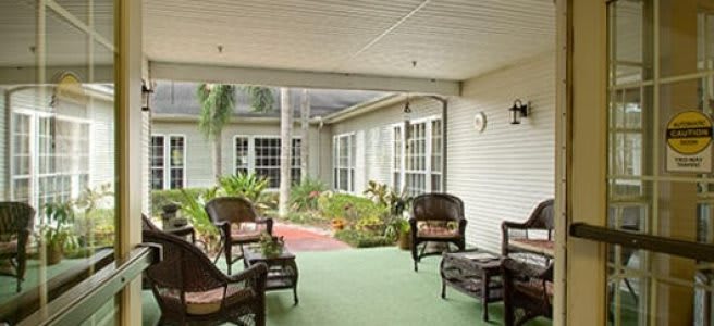 A cozy outdoor patio area with wicker chairs and a small table surrounded by greenery.