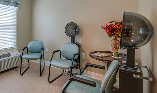 A quiet waiting room featuring comfortable chairs, a small table with decorative flowers, and a fan for ventilation.