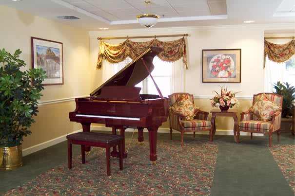 A cozy living room features a grand piano, elegant furniture, and tasteful artwork.