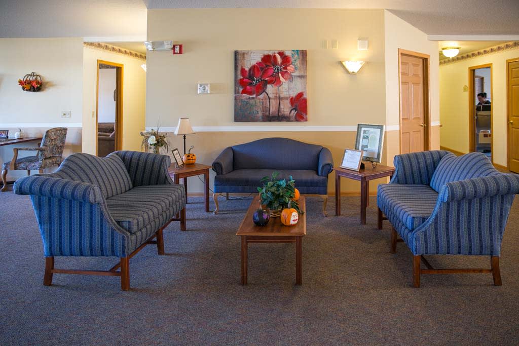 A well-furnished waiting room with sofas, chairs, and tables, accented by a painting and potted plants.