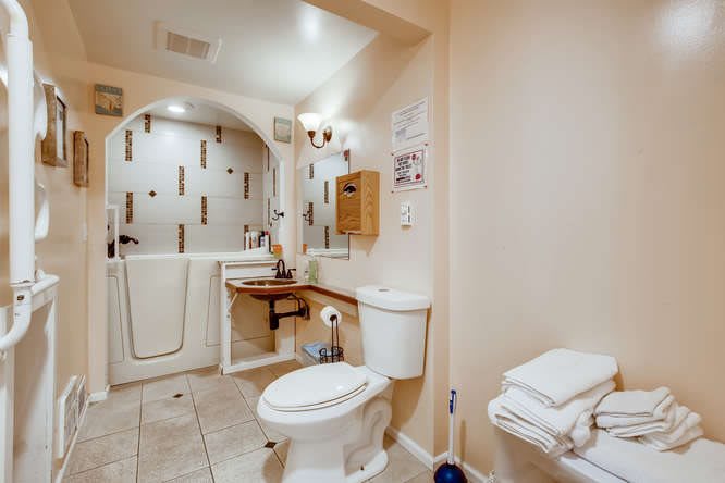An accessible bathroom featuring a walk-in tub, toilet, and sink with towels neatly arranged.
