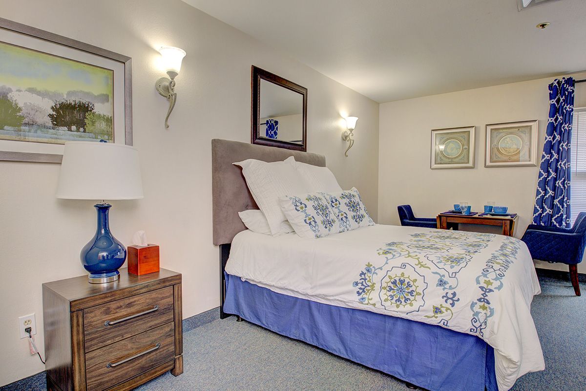 A cozy bedroom with a neatly made bed, adorned with blue and white bedding, accompanied by a bedside table with a lamp.