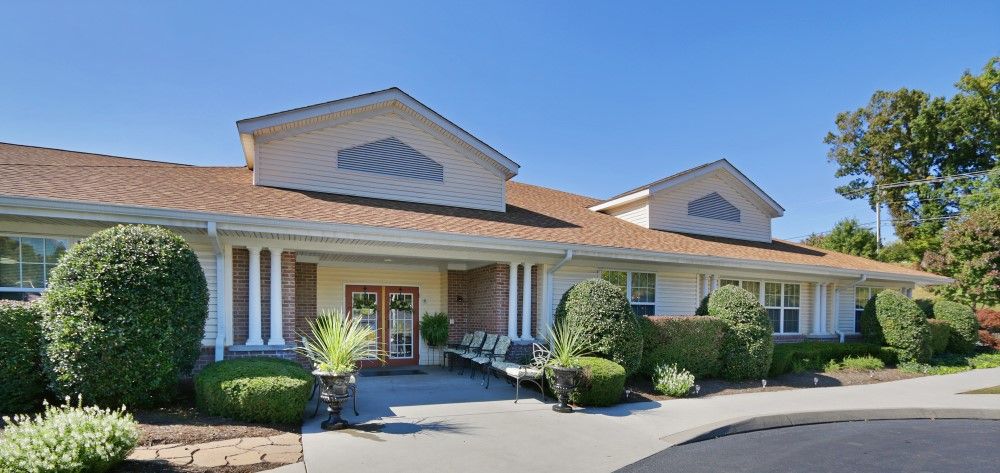 A well-maintained building entrance with neatly trimmed bushes and outdoor seating.