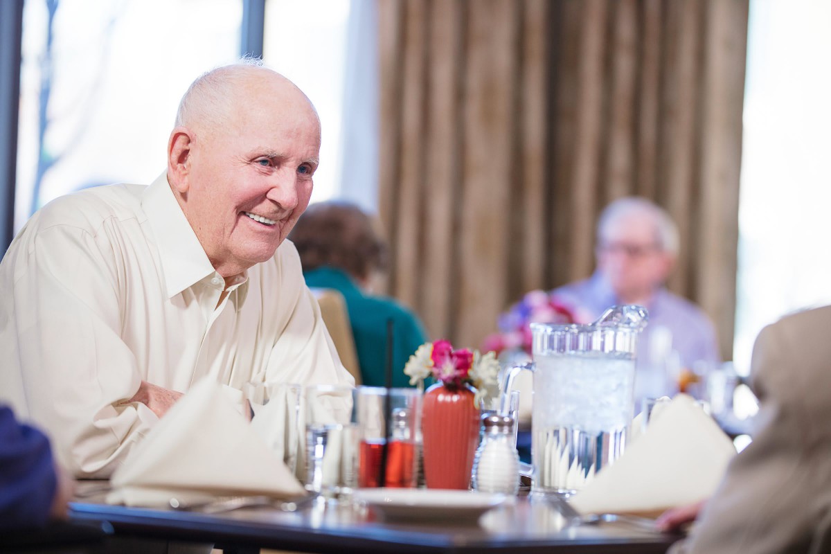 An elderly man smiling while dining at a restaurant.