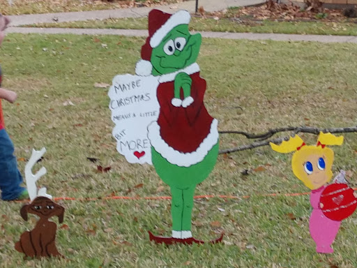 A cheerful holiday decoration featuring the Grinch in a Santa outfit, holding a list.