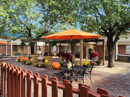 A cozy outdoor dining area with an orange umbrella, surrounded by trees and decorated for autumn.