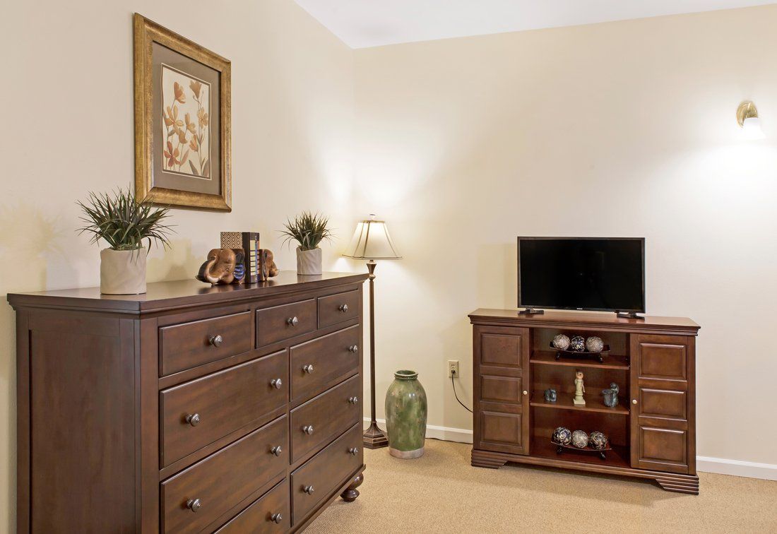 A cozy bedroom with dark wood furniture, including a dresser and TV stand, complemented by decorative items and a floor lamp.