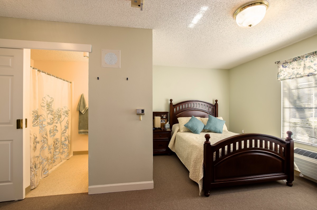 A cozy bedroom with a wooden bed and nightstand, adjacent to a bathroom.