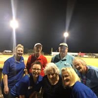 A group of people posing together under bright lights at a sports field during nighttime.