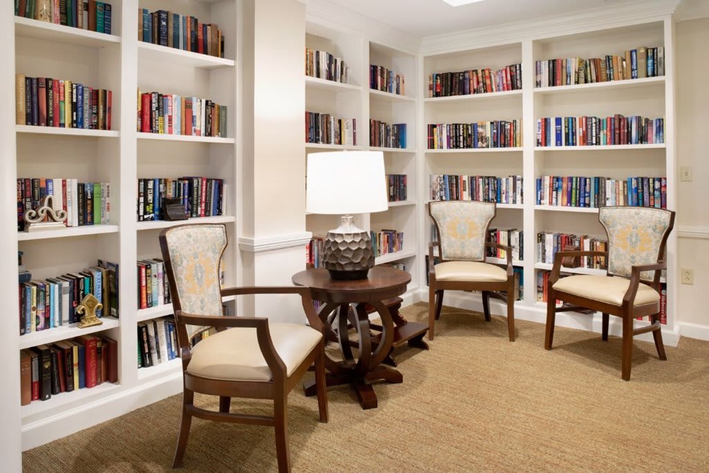 A cozy reading nook with bookshelves, chairs, and a table with a lamp.