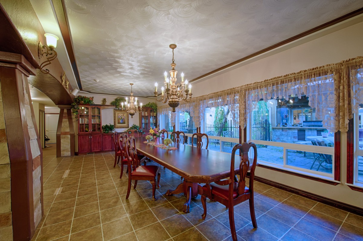 A spacious dining room featuring a long wooden table with matching chairs, illuminated by chandeliers and surrounded by large windows.