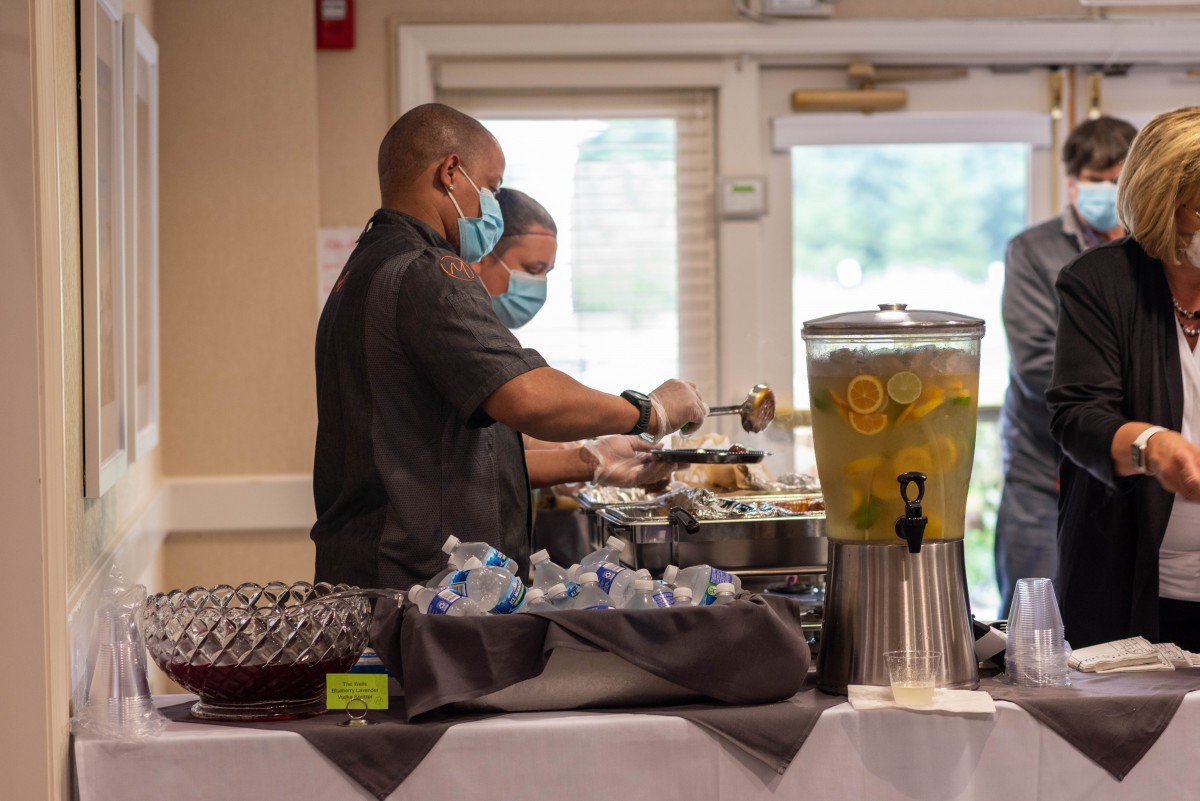Caterers wearing masks serve food at a buffet during an indoor event.