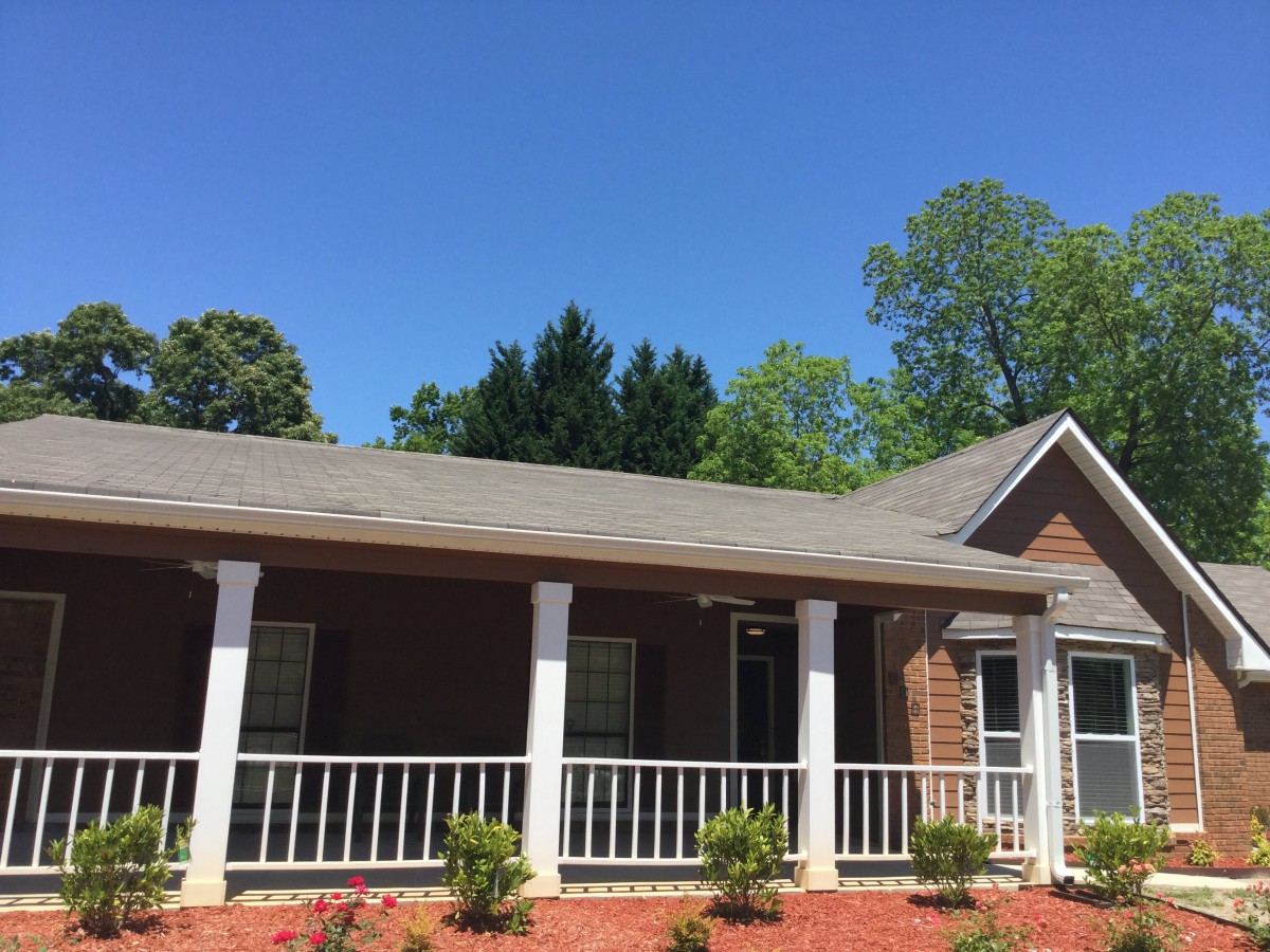 A single-story brick house with a front porch and landscaped yard under a clear blue sky.
