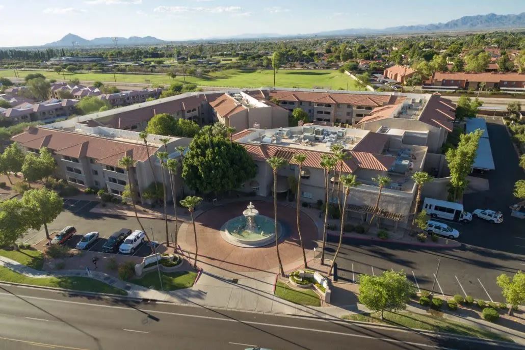 Aerial view of a building complex surrounded by palm trees and featuring a central fountain.
