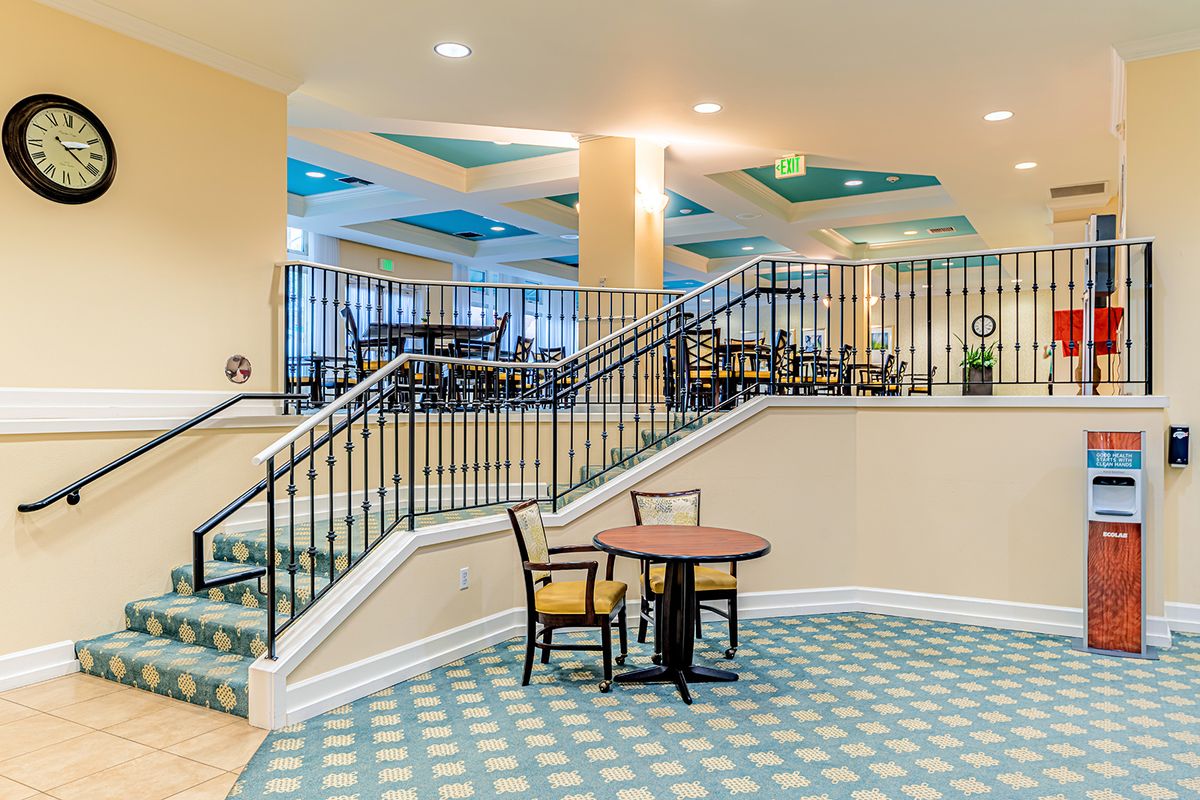A spacious interior with a staircase leading to a dining area, featuring patterned carpet and elegant railings.